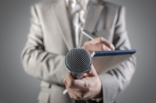 Journalist or news reporter at a press conference or media event holding a microphone and writing notes