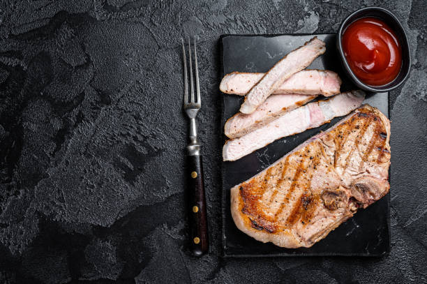 istock Grilled slised pork Chop or T-bone meat steak. Black background. Top view. Copy space 1466992587
