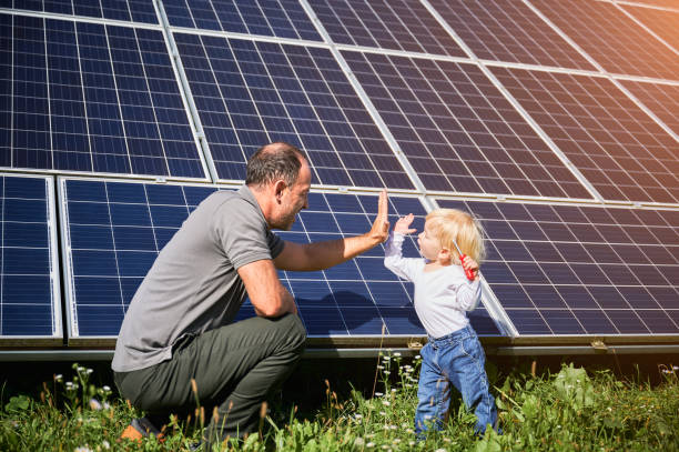Little son and his smiling father giving each other high-five on background of solar panels stock photo