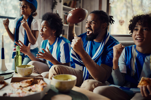 Cheerful African American family celebrating success of their soccer team while watching a game on TV at home.