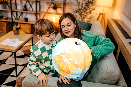 Little boy sitting on couch with his mother looking at globe