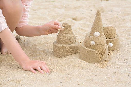 Child decorating sand castle with shell on beach, closeup