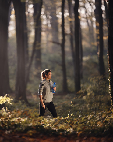 Young female athlete taking a break after sports training during autumn day in the forest. Copy space. Photographed in medium format.