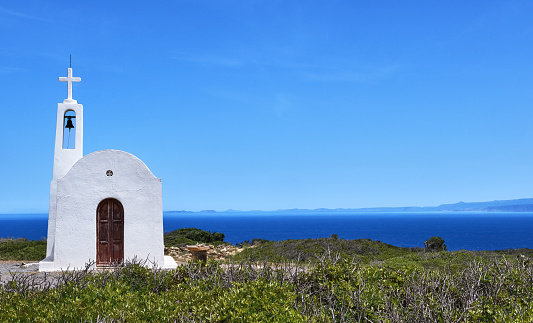 White Greek Orthodox chapel or church on hilltop of seashore against clear blue sky on sunny day. Traditional religious building. Typical Greek landscape. Frontal shot.