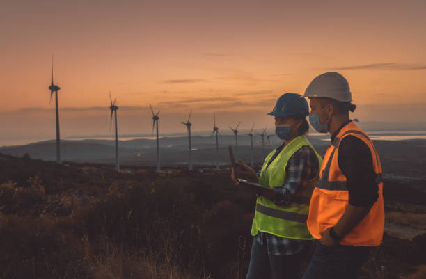 istock Maintenance engineer team with face mask working in wind turbine farm at sunset during pancemic 1467016253