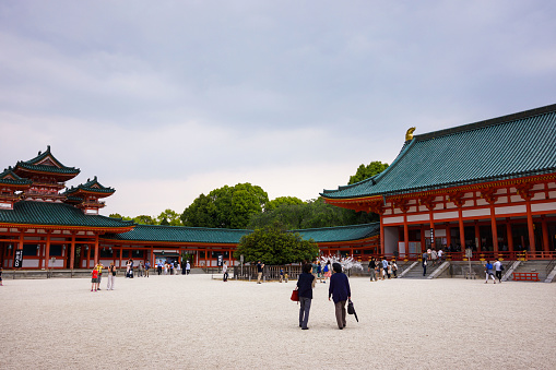 Kyoto, Japan - May 2014: View of the inner courtyard of Heian Shrine with crowd of people walking with main prayer hall, Byakko-rou tower and cloudy sky background.