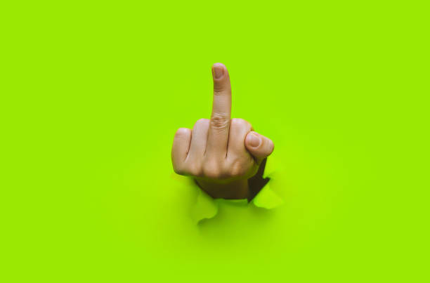 Middle finger of left hand, insulting gesture. Torn hole in green paper. Fuck you concept. Aggressive reaction. stock photo