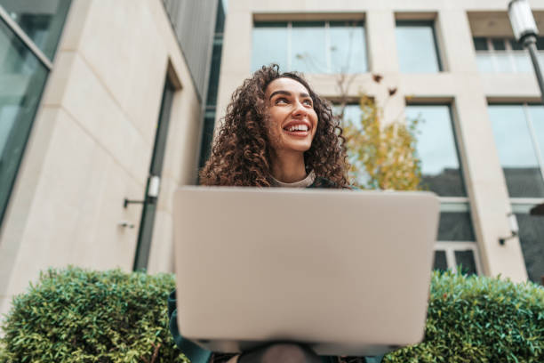 istock Young woman using laptop while sitting by the building outdoors. 1467021410
