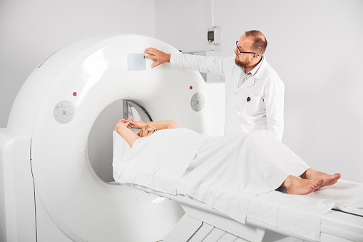 Medical computed tomography or MRI scanner. Male radiologist presses MRI button to examine female patient.