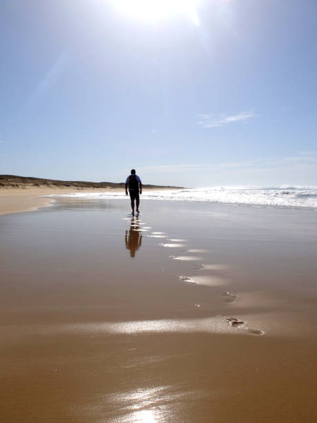 istock Footprints on sandy beach leading to man in silhouette walking. Vertical format. 1467023558