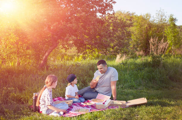 dad with children sit on a picnic under a tree