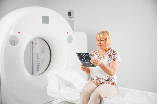 Female patient holding results of medical computed tomography or MRI. Medical computed tomography or MRI scanner. Patient making MRI, sitting on couch. Blonde woman holding MRI result, scan, x-ray, looking, examining, thinking. Concept of medicine and healthcare. x ray results stock pictures, royalty-free photos & images