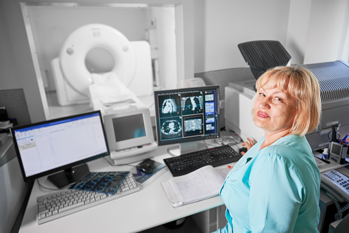 Medical computed tomography or MRI scanner. Portrait of female nurse working at computer, making MRI. Woman wearing blue uniform. Concept of medicine and hospital.