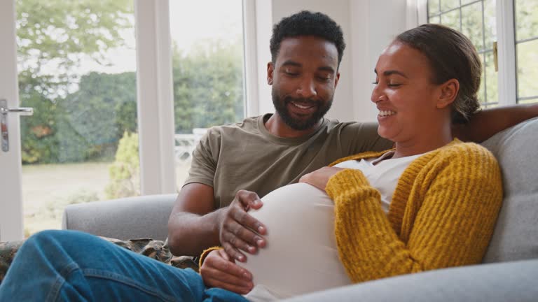 Pregnant army couple with woman sitting next to husband as he touches her stomach - shot in slow motion