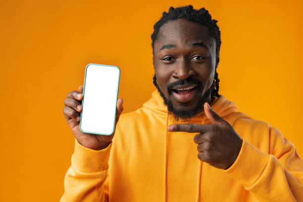 istock Smiling african man pointing at cellphone with blank screen with copy space 1467030170