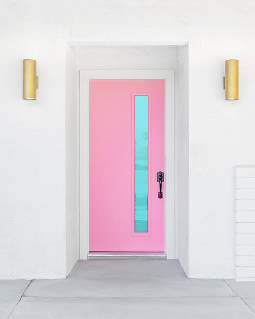Pink Door with a vertical blue window on a white mid-century modern home in Palm Springs, California. Gold porch lights on each side of the entryway.