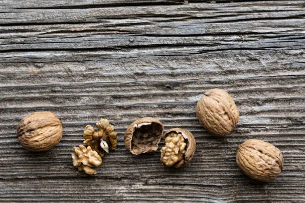 top view, on an old wooden board, in the foreground, some walnuts with and without shell. Copy space.
