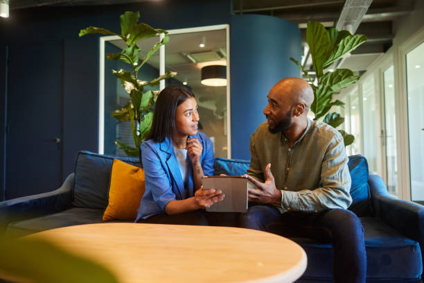 Businesspeople talking over a tablet while sitting on an office sofa