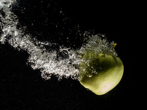 Green apple falling in water