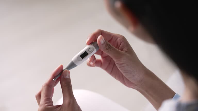 Young Asian woman looking at thermometer checking temperature.