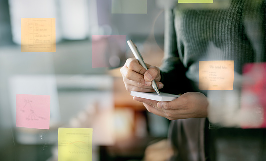 Closeup image of businesswoman hands writing plan on sticky note.