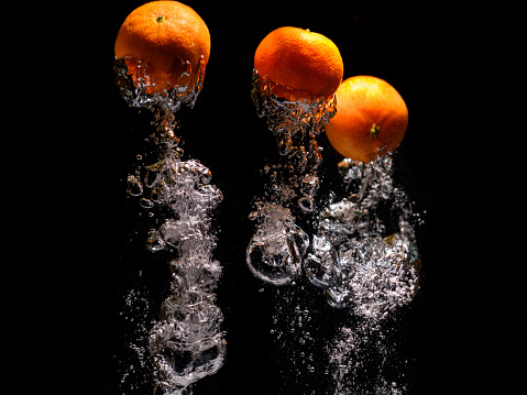 tangerines falling into water with splash on black background