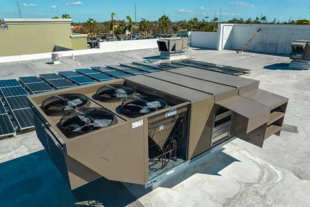 Photo of External unit of commercial air conditioning and ventilation system installed on industrial building roof. Exhaust vent on flat factory rooftop