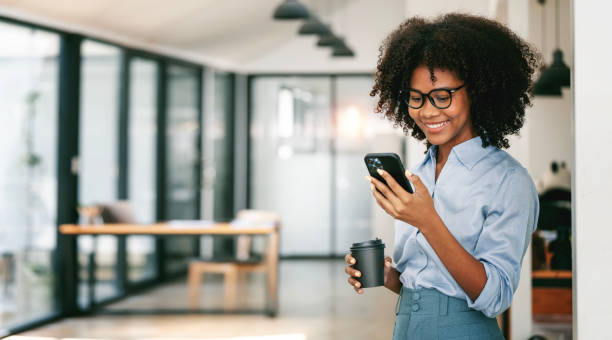 Beautiful smiling curly-haired businesswoman using smartphone in office, copy space.