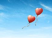 Heart shaped red balloons on blue sky.
