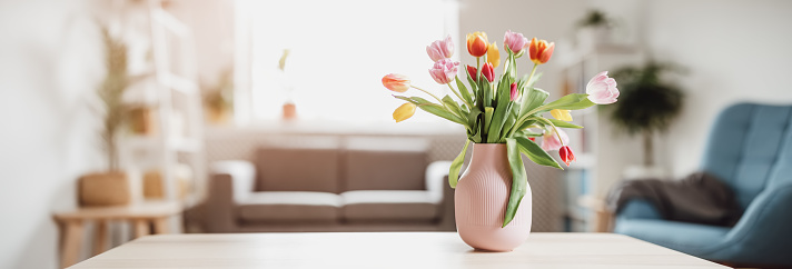 A bunch of tulips in pink vase standing on the wooden table indoors. Concept of the Mother's and Valentine's day and Easter.