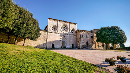 The beautiful facade of the Abbey Church of San Pietro in the medieval heart of Assisi in Umbria, central Italy. Built in Romanesque and Gothic style in the 10th century by the Benedictines, the facade was made of red stone from the nearby Monte Subasio. It has a rectangular shape with three entrance portals and three rose windows. The large central portal is surmounted by an arch and a larger rose window. Famous for being the city of San Francesco and Santa Chiara (St Francis and St Clare), Assisi is recognized in the world as a place of spirituality and peace between all peoples and different confessions. The Umbria region, considered the green lung of Italy for its wooded mountains, is characterized by a perfect integration between nature and the presence of man, in a context of environmental sustainability and healthy life. In addition to its immense artistic and historical heritage, Umbria is famous for its food and wine production and for the high quality of the olive oil produced in these lands. Since 2000 the Franciscan sites of Assisi have been declared a World Heritage Site by UNESCO. Super wide angle image in 16:9 format and high definition quality.