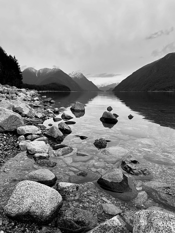 Calm lake with mountains and rocks reflecting on the water like a mirror. Low angle, black and white