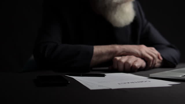 Risky elderly boss with grey beard signing contract at table, business decision