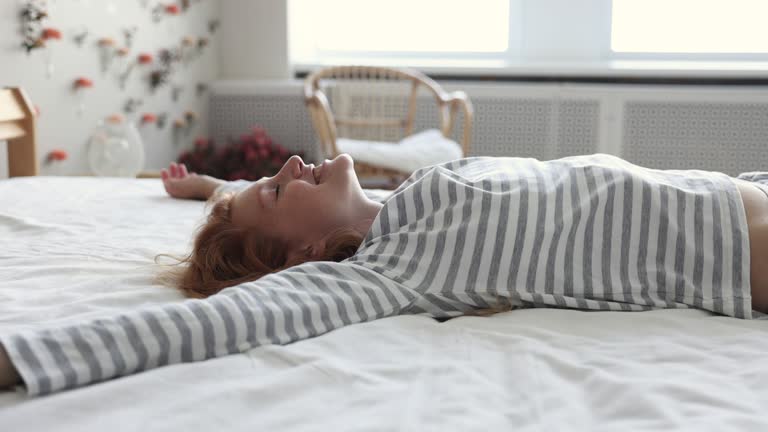 Young woman falls on bed with arms raised feels happy