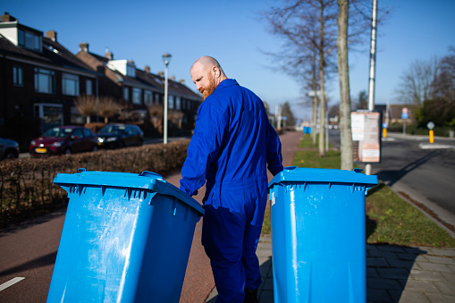 Handsome redhead Worker organising the blue bins at a plastic recycling station in a local neighbourhood