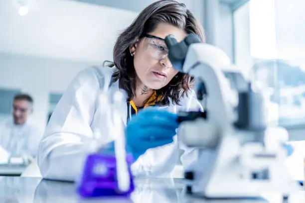 Photo of Adult female student analyzing liquid under microscope