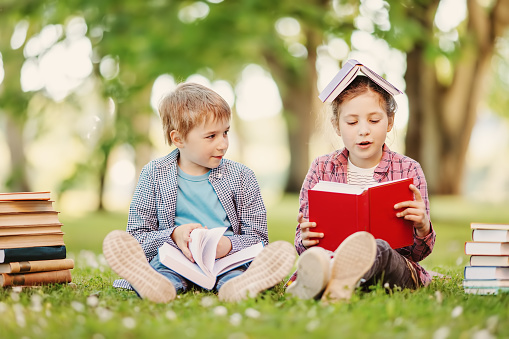 Boy and girl sitting on the meadow with books in their hands. Concept of the back to school and hobby.