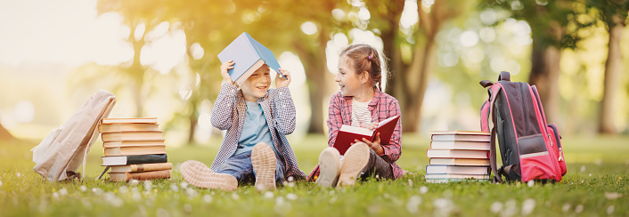 Boy and girl sitting on the meadow with books in their hands. Concept of the back to school and hobby.