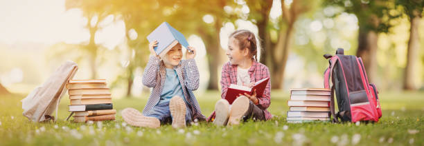 Boy and girl sitting on the meadow with books in their hands. stock photo