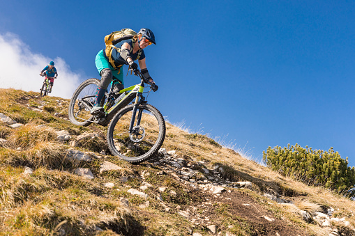 An experienced and well equiped mountainbike couple is riding down a narrow single trail on a sunny autumn day in the mountain region nearby Lake Garda. This area is very famous for mountainbiking during summertime.\nCanon EOS 5D Mark IV, 1/1000, f/2,8 , 35 mm.