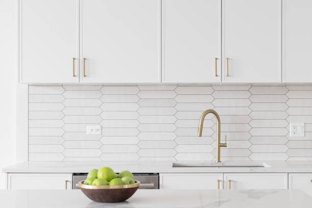 istock A kitchen detail with white cabinets, gold faucet, and tiled backsplash. 1467058837