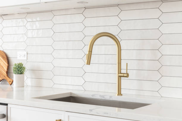 istock A kitchen detail with white cabinets, gold faucet, and tiled backsplash. 1467058862