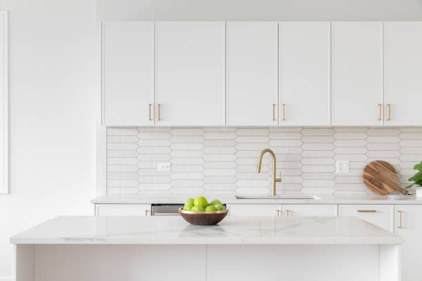 A kitchen detail with white cabinets, gold faucet, and tiled backsplash. A beautiful kitchen faucet detail with white cabinets, a gold faucet, white marble countertops, and a brown picket ceramic tile backsplash. cleaning cupboard stock pictures, royalty-free photos & images