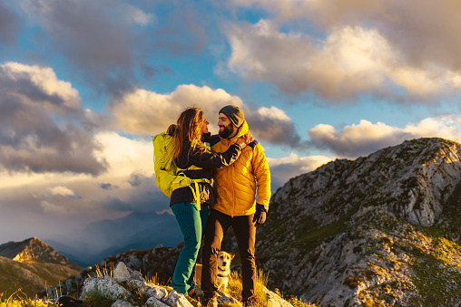 couple of mountaineers in love hug each other on top of a mountain at sunset. hikers with backpacks summiting a peak.