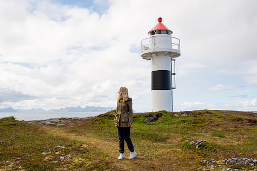 Woman walks near the lighthouse and enjoy beautiful nature landscape. Lonely girl. Amazing scenic outdoors view in North. Travel and adventure. Explore Norway. Lofoten Islands. Scandinavia