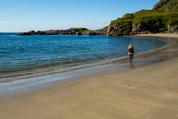istock Young woman with a backpack walks along an empty sandy ocean beach. Town and mountains. Beautiful nature landscape. Lonely girl. Wanderlust. Travel, adventure, lifestyle. Explore North, Norway 1467062741