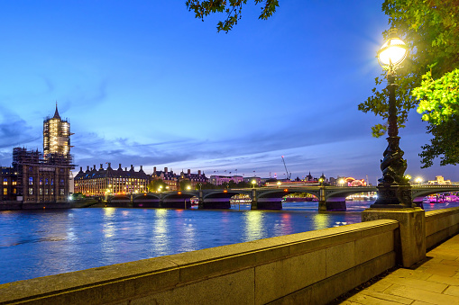 View of Westminster and the River Thames in London, UK. The Houses of Parliament and Big Ben are to the left. A red bus crosses Westminster Bridge.