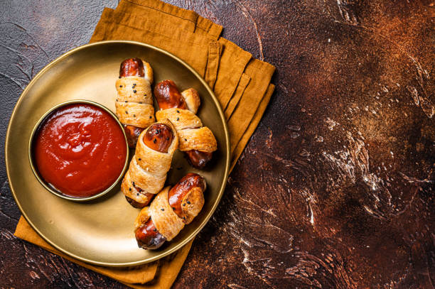 ケチャップとパイ生地で焼いたロールホットドッグソーセージ。暗い背景。平面図。スペースをコピーする - blanket pig hot dog sausage ストックフォトと画像