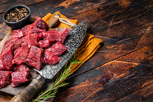 Sliced Raw venison dear meat for a stew, game meat on butcher cutting board. Wooden background. Top view. Copy space.
