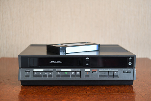 An old vintage videotape recorder from the 1980s stands on a dark table with a videotape. Retro VCR.